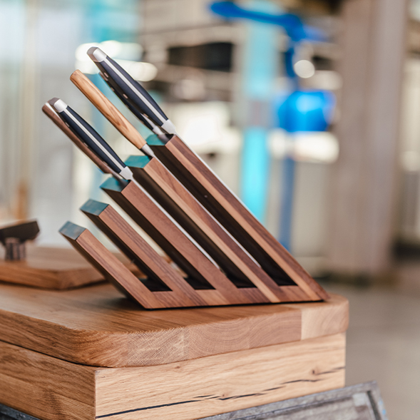 Auf einem Holztisch steht seitlich ein Holz-Messerblock mit Messern bestückt.